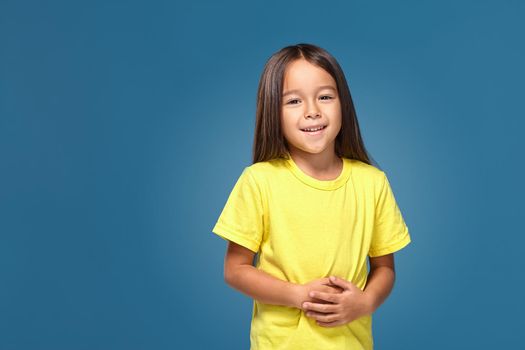 Little girl in yellow t-shirt is smiling on blue background