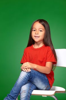 little girl wearing red t-short and posing on chair on green background