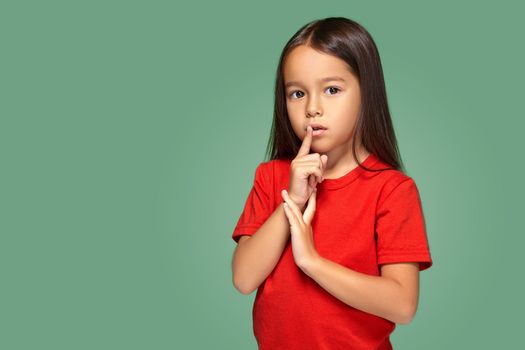 girl placing finger on lips asking shh, quiet, silence on green background