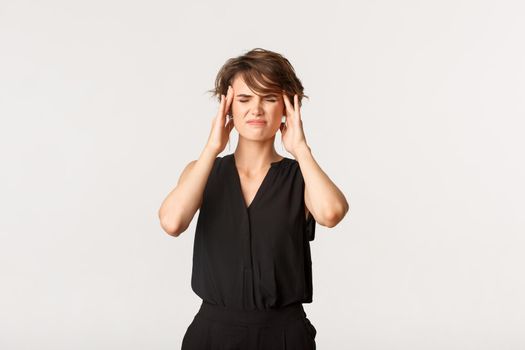 Young businesswoman touching temples and grimacing from painful migraine. Girl complaining on headache, standing white background.