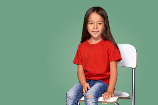 little girl wearing red t-short and posing on chair on green background