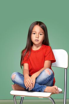 little girl wearing red t-short and posing on chair on green background