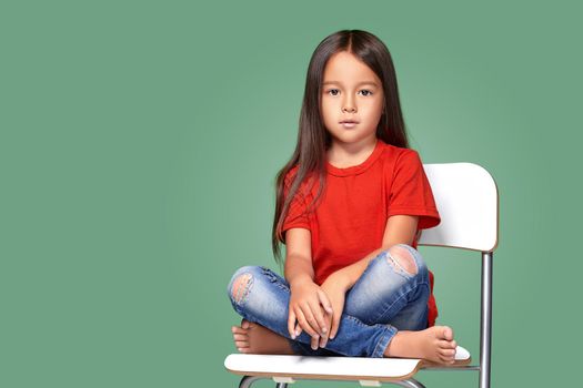 little girl wearing red t-short and posing on chair on green background