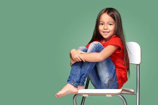 little girl wearing red t-short and posing on chair on green background