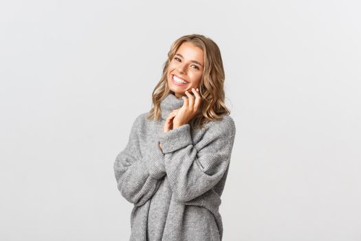 Portrait of tender smiling woman, looking happy and laughing, gently touching face, standing over white background.