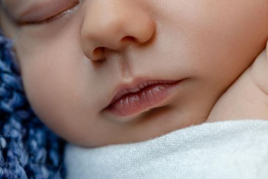 Newborn - baby, face close-up. The sleeping Newborn boy under a white knitted blanket lies on the blue fur. Newborn. 14 days.