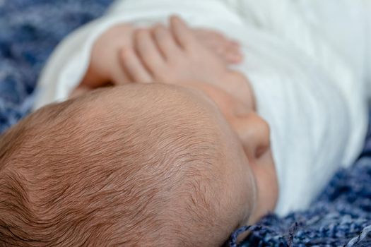 Newborn - baby, face close-up. The sleeping Newborn boy under a white knitted blanket lies on the blue fur. Newborn. 14 days.