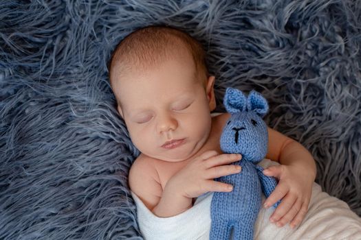 Newborn baby boy in bed. New born child sleeping under a white knitted blanket. Children sleep. Bedding for kids. Infant napping in bed. Healthy little kid shortly after birth. Cable knit textile.