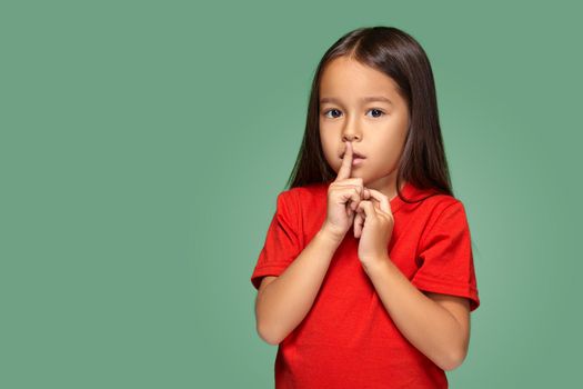 girl placing finger on lips asking shh, quiet, silence on green background