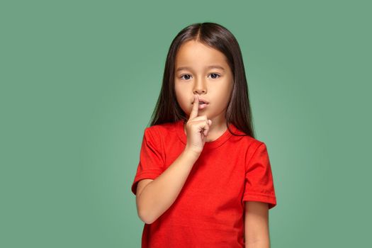 girl placing finger on lips asking shh, quiet, silence on green background
