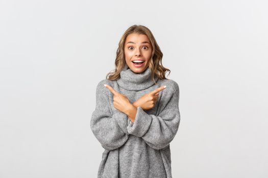 Young attractive woman with blond short hairstyle, pointing fingers sideways, showing left and right variants, looking excited and happy, standing over white background.