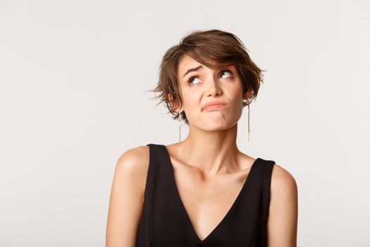 Close-up of indecisive girl looking upper left corner, shrugging clueless, standing over white background.