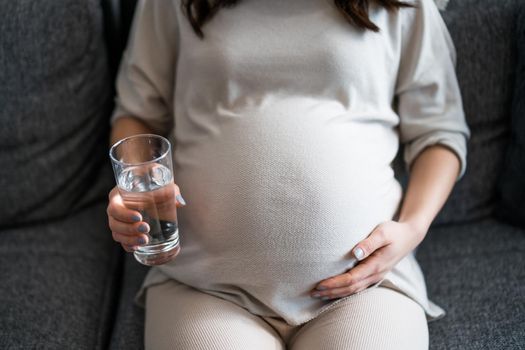 Pregnant woman relaxing at home. She is sitting on bed and drinking water.