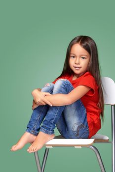 little girl wearing red t-short and posing on chair on green background