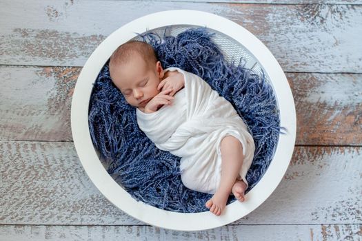 Little baby boy sleeping in a basket on the wooden floor, studio shot. Newborn. 14 days