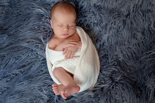 Newborn baby boy in bed. New born child sleeping under a white knitted blanket. Children sleep. Bedding for kids. Infant napping in bed. Healthy little kid shortly after birth. Cable knit textile.