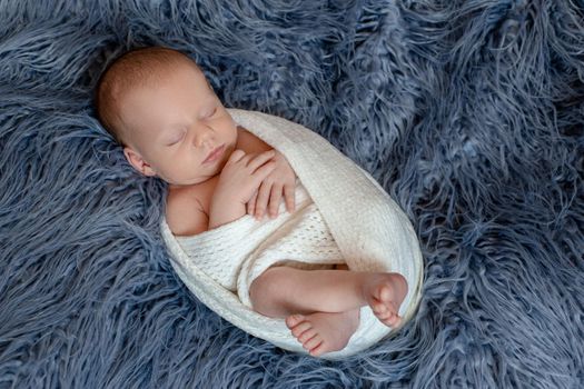 Newborn baby boy in bed. New born child sleeping under a white knitted blanket. Children sleep. Bedding for kids. Infant napping in bed. Healthy little kid shortly after birth. Cable knit textile.