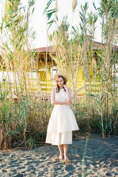 Young woman stands barefoot on the sand with a reed branch in her hand. High quality photo