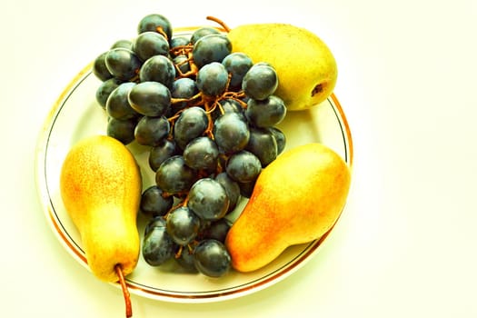 the sweet and fleshy product of a tree or other plant that contains seed and can be eaten as food. Porcelain plate with a golden border with ripe delicious grapes and pears.