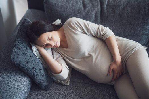 Pregnant woman is relaxing. She is lying on bed at home.