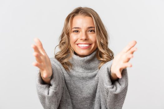 Close-up of lovely blond girl smiling, stretching hands forward to catch or hold something, standing over white background.