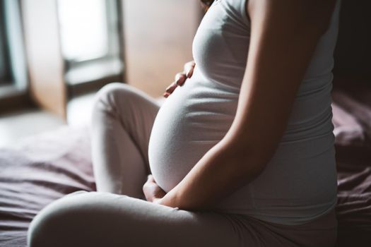 Pregnant woman relaxing at home. She is sitting on bed in bedroom.