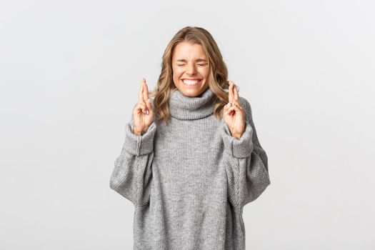 Image of beautiful hopeful woman begging, crossing fingers and making wish, standing over white background.