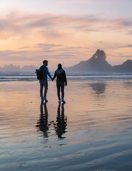 a couple of men and women mid-age watching the sunset on the beach of Tofino Vancouver Island Canada, beautiful sunset on the beach with pink-purple colors in the sky. Canada Tofino Vancouver Island