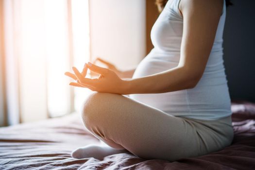 Pregnant woman relaxing at home. She is sitting on bed and meditating.