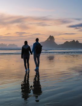 a couple of men and women mid-age watching the sunset on the beach of Tofino Vancouver Island Canada, beautiful sunset on the beach with pink-purple colors in the sky. Canada Tofino Vancouver Island