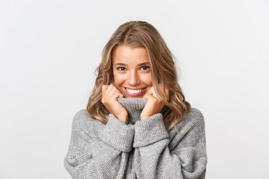 Close-up of lovely blond girl, smiling silly and looking coquettish at camera, standing over white background.