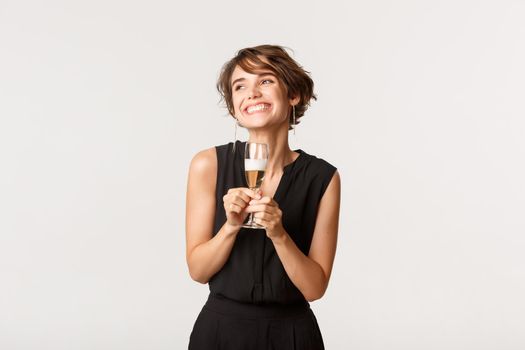 Gorgeous elegant woman smiling and holding glass of champagne, standing over white background.