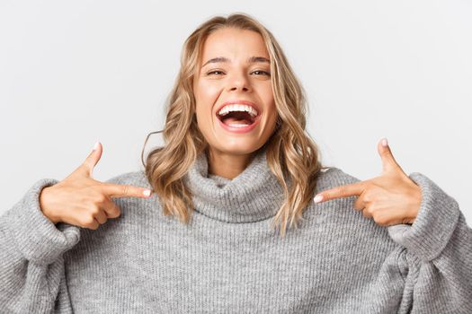 Close-up of happy attractive blond girl laughing, smiling and pointing fingers at your logo, standing over white background.