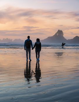 a couple of men and women mid-age watching the sunset on the beach of Tofino Vancouver Island Canada, beautiful sunset on the beach with pink-purple colors in the sky. Canada Tofino Vancouver Island