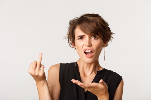 Woman complaining, looking confused and showing finger without wedding ring, standing over white background.