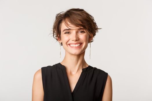 Close-up of stylish smiling businesswoman looking happy at camera, standing over white background.