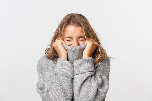 Close-up of happy blond girl, pulling sweater on face and smiling cheerful, standing over white background.