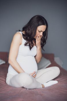 Pregnant woman is having pain in her stomach. She is sitting on bed at home.