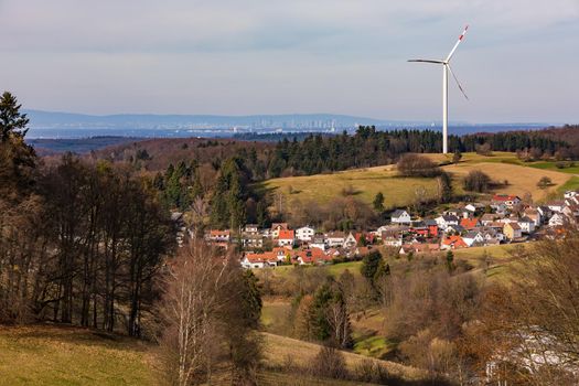 A rural landscape with a village, a wind turbine and the distant view of the city of Frankfurt