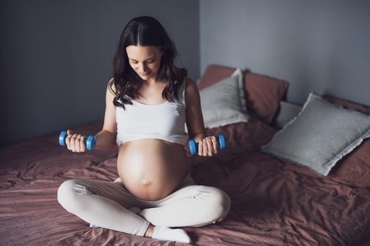 Pregnant woman is exercising with weights at home.