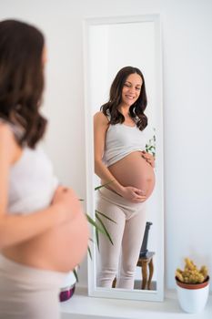 Happy pregnant woman is looking at her stomach in mirror at home.