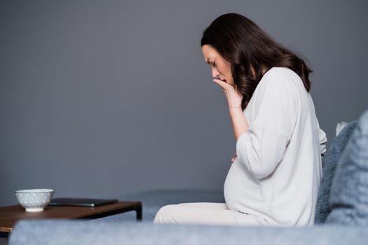 Pregnant woman is having pain in her stomach and back. She is sitting on bed at home.