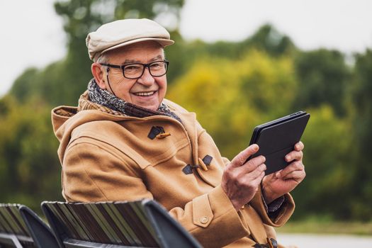 Outdoor portrait of cheerful senior man in winter coat who is using digital tablet.