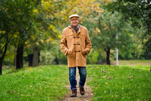 Happy senior is walking in park in autumn.