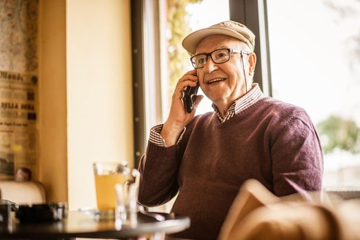 Senior man is sitting in cafe and talking on phone.