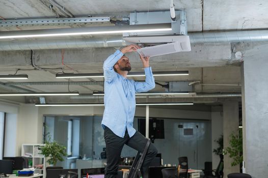 Caucasian bearded man repairing the air conditioner in the office