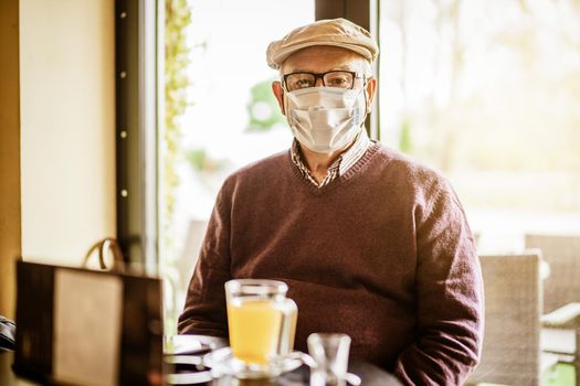 Senior man is sitting in cafe with face protection mask. Covid 19 prevention concept.