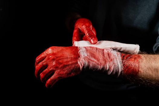 A man covered in blood bandages his hands