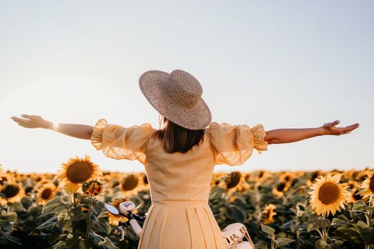 Woman with open arms in sunflowers field. Yellow colors, warm toning. Free girl in straw hat and retro dress. Vintage timeless fashion, amazing adventure, countryside, freedom scene.High quality photo