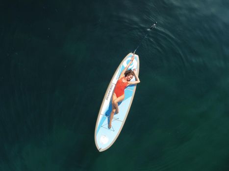 Young attractive brunette woman in red swimsuit, swimming on kayak around volcanic rocks, like in Iceland. Back view. Christmas holiday vacation and travel concept.